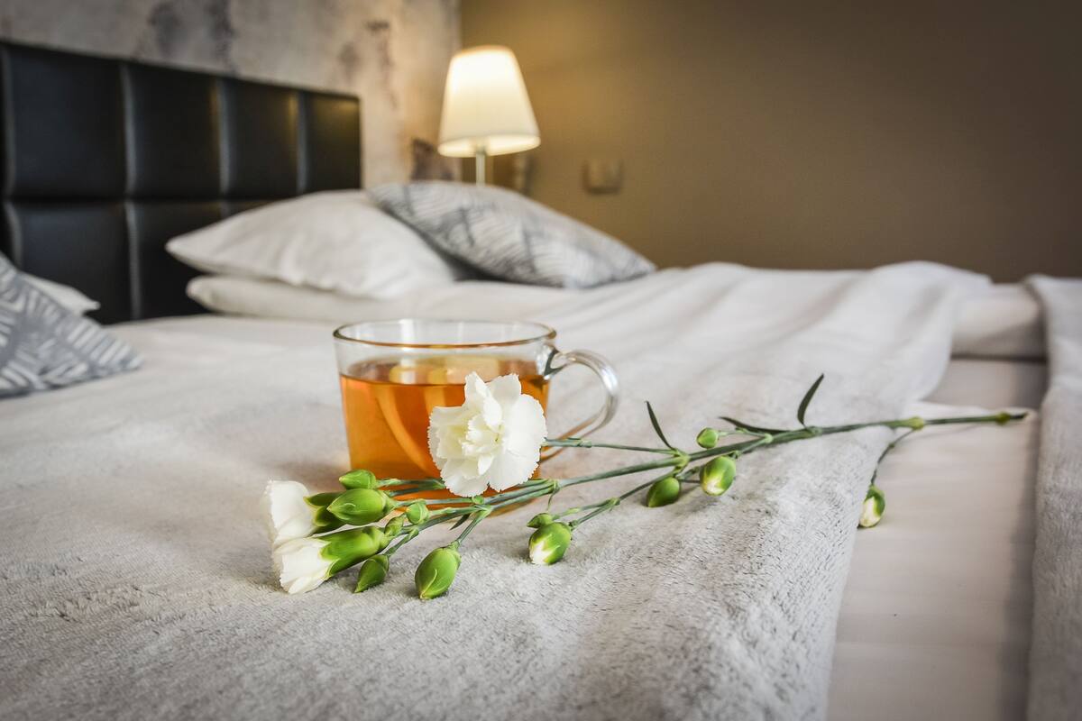 A bed with a cup of tea, white flowers, and green buds on a textured blanket.