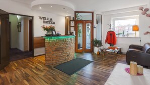 A reception area with a brick counter, a coat hanging rack, a leather sofa, and a window with a view. - Willa Bryza (Gdynia)