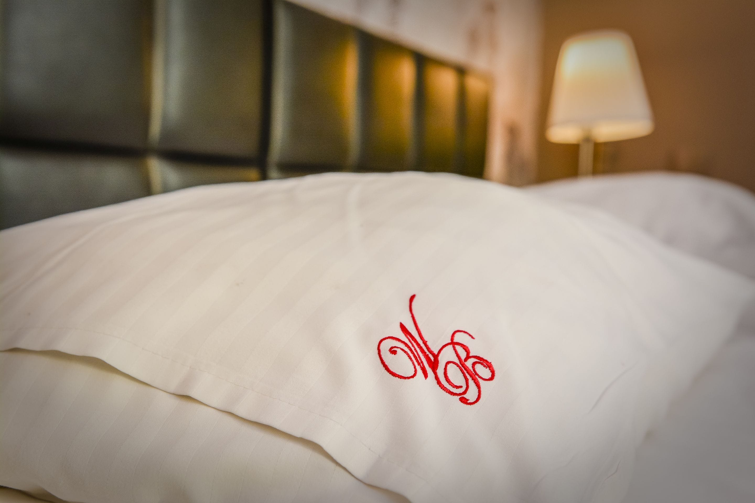 A bed with a white pillow featuring a red embroidered design.