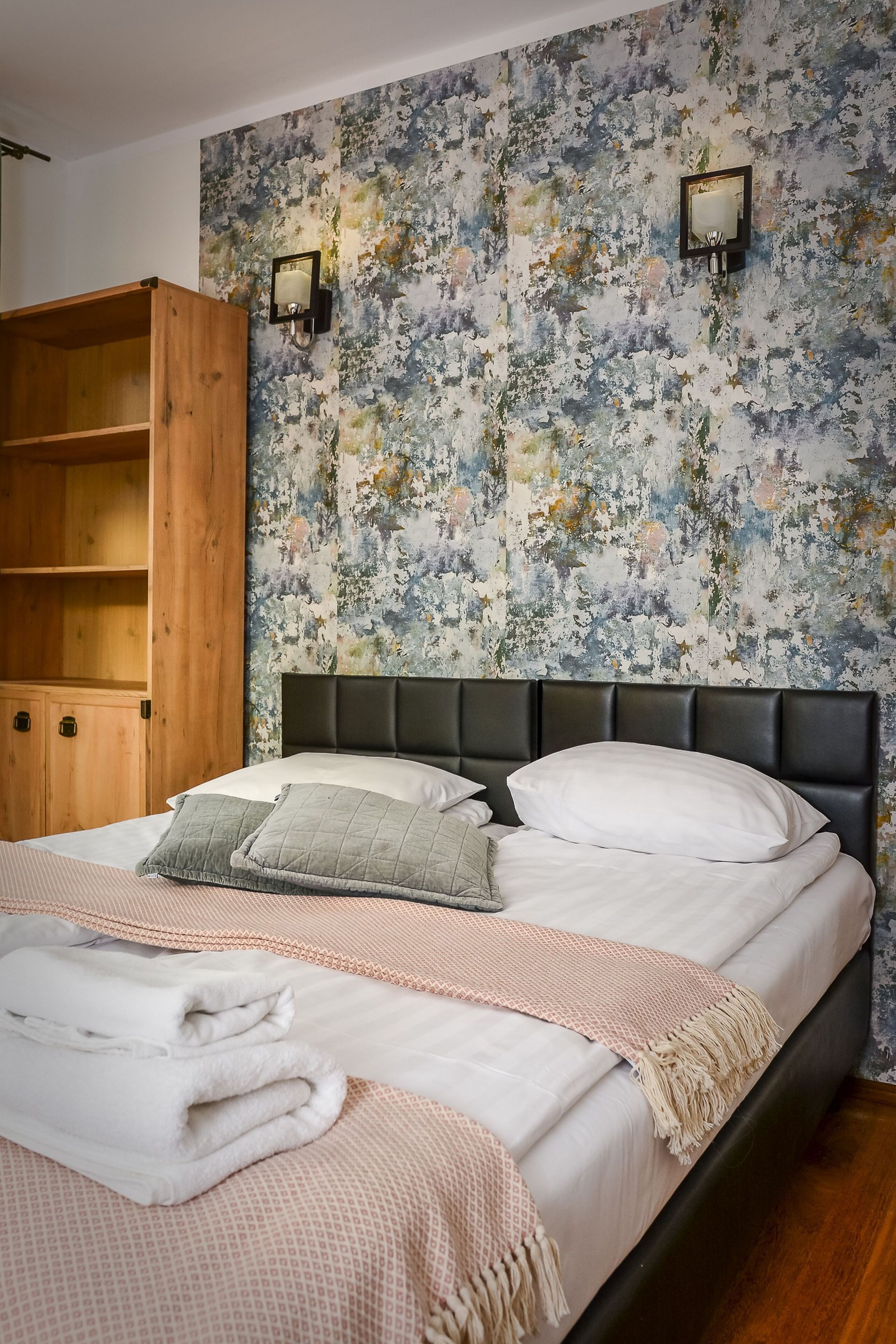 A bedroom with a bed, wooden wardrobe, and a floral-patterned wall.