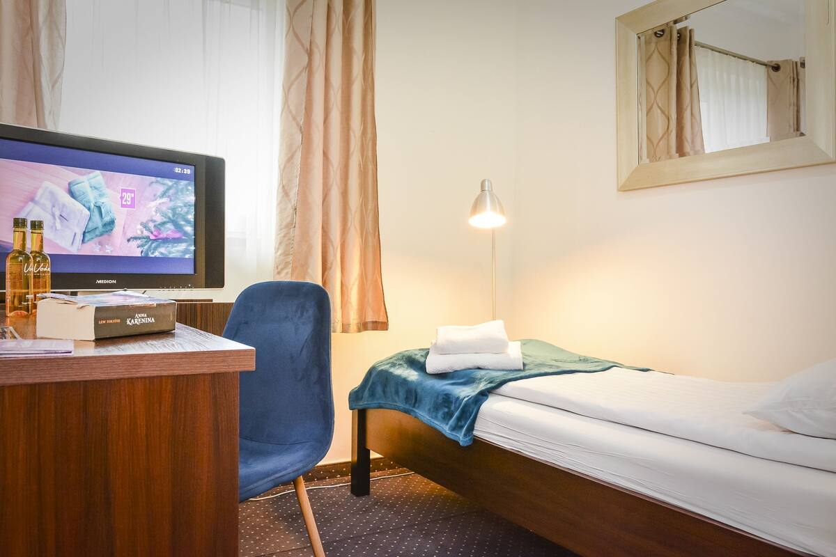 A hotel room with a bed, a desk, a chair, a TV, and a lamp.