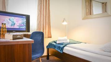 A hotel room with a bed, a desk, a chair, a TV, and a lamp.