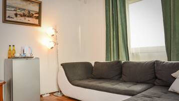 A living room with a grey sofa, a small white fridge, and a painting on the wall.
