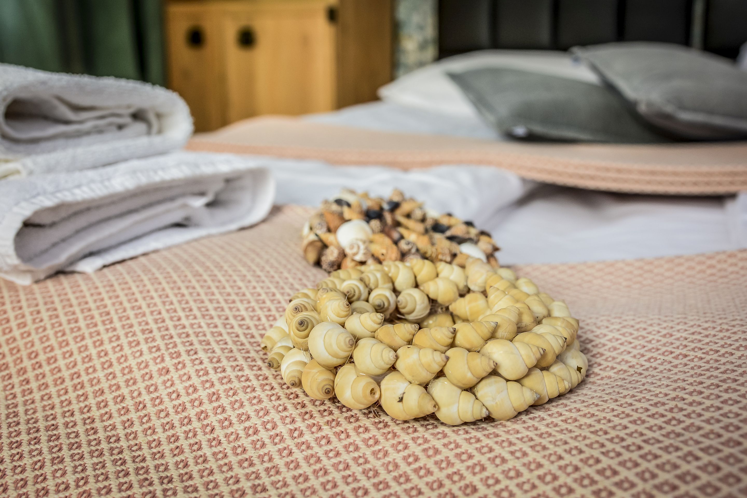 Una cama con toallas blancas dobladas con cuidado y una pila de objetos pequeños, color beige y en forma de espiral, sobre un edredón estampado.