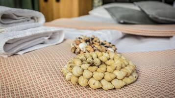 Una cama con toallas blancas dobladas con cuidado y una pila de objetos pequeños, color beige y en forma de espiral, sobre un edredón estampado.