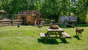 A rustic wooden structure with a picnic table in a grassy area, surrounded by trees and a wooden cart. - Camping Saint Michel (Courtils)