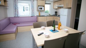 A compact kitchen with a microwave, refrigerator, and a dining area with a table and chairs. - Camping Saint Michel (Courtils)