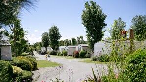 A residential street with single-story houses, a clear sky, and a person walking. - Camping Saint Michel (Courtils)