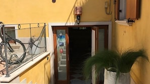 A yellow building with a staircase leading to an entrance, a bicycle parked on the left, and a potted plant in the foreground. - Relais Sweet Days (Peschiera del Garda)