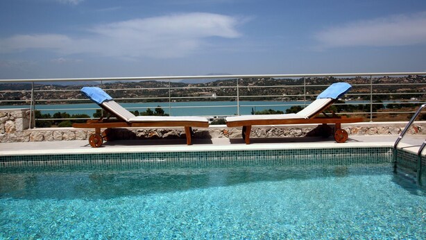 A pool with two lounge chairs and a view of a lake and hills. - Edem Resort (Ermionida)