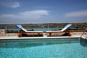 Una piscina con dos sillas de descanso y vista a un lago y colinas.