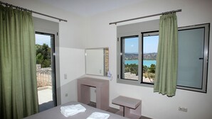 A hotel room with a bed, a vanity with a mirror, a window with a view of the sea, and a balcony with green curtains. - Edem Resort (Ermionida)