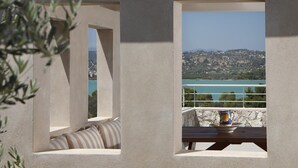 A balcony with a stone wall, a cushioned bench, and a table with a bowl and a cup. - Edem Resort (Ermionida)