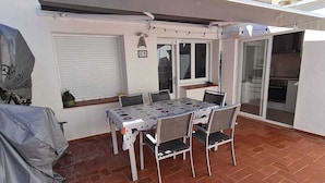 Un patio con tavolo e sedie, condizionatori, una zona coperta e una porta scorrevole in vetro.