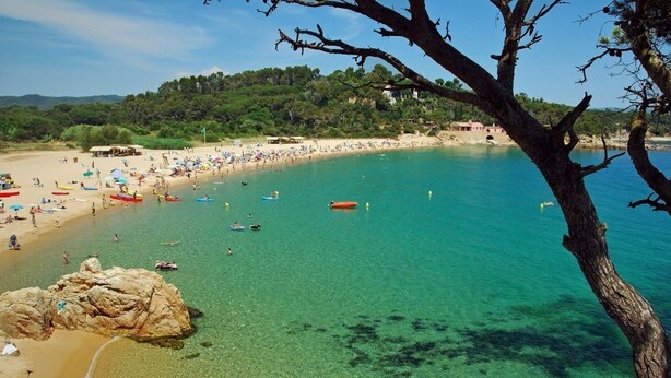 Una spiaggia con acque turchesi cristalline, persone che nuotano e barche.