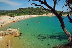 A beach with clear turquoise water, people swimming, and boats.