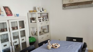 Un'area pranzo con un tavolo ricoperto da una tovaglia a righe, circondato da sedie. Si nota a sinistra un mobile con ante e ripiani in vetro.