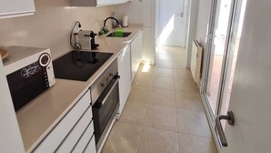Una cucina moderna con mobili bianchi, forno integrato e microonde. Si vede una finestra a destra e una porta che dà su un'altra stanza.