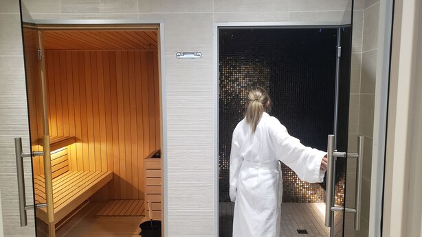 Una sala de sauna con bancos de madera y una puerta de cristal que da a una zona con azulejos.