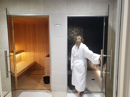A sauna room with wooden benches and a glass door leading to a tiled area.