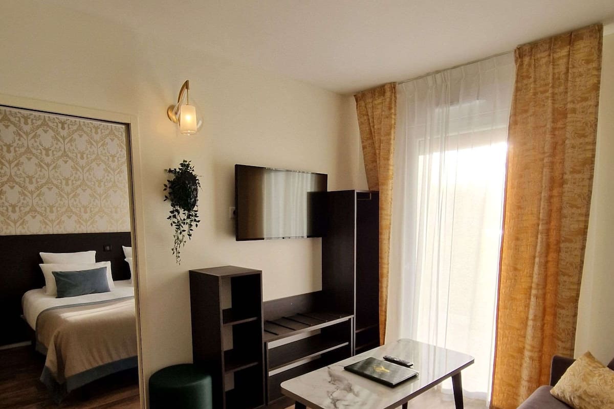 A modern hotel room with a bed, a sofa, a TV, and a small table.