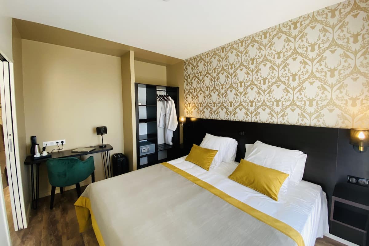 A hotel room with a bed, bedside table, desk, chair, and a wardrobe.