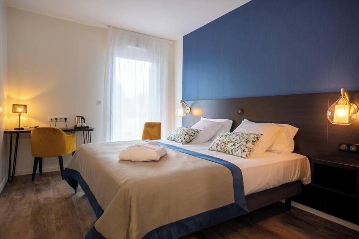 A hotel room with a bed, bedside tables, a desk, a chair, and a window with curtains.