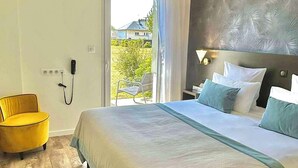 Un dormitorio con una cama grande, un sillón amarillo, una mesita de noche con lámpara y vistas al exterior.