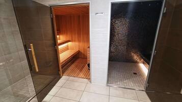 A sauna room with wooden benches and a tiled floor, adjacent to a glass-enclosed shower area.