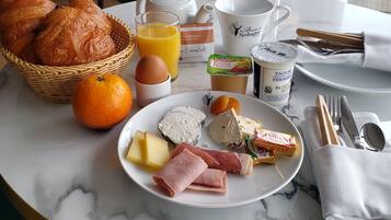 Una mesa de desayuno con cruasanes, jugo de naranja, queso, jamón y pan.