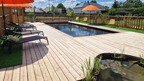 Una terraza de madera con piscina, sillas de descanso y un pequeño estanque con nenúfares.