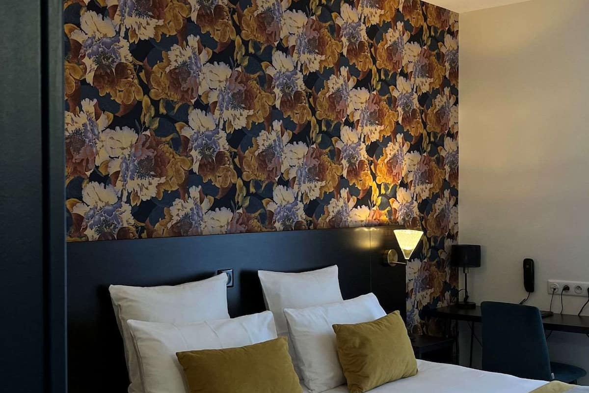 A hotel room with a large bed, a floral wallpaper, a nightlight, and a desk with a chair.