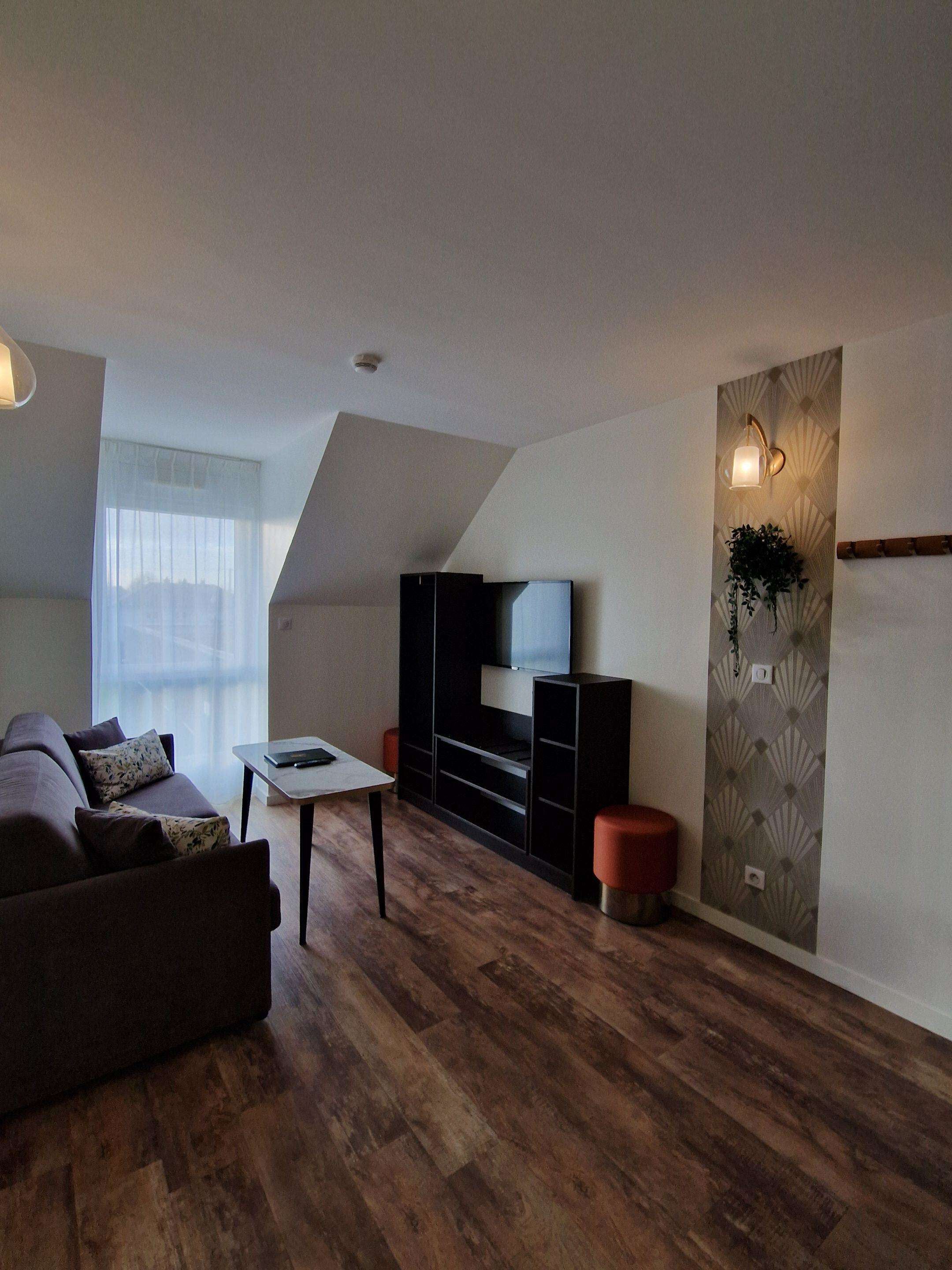 A modern living room with a dark brown sofa, a small white table, and a black entertainment unit with a TV.