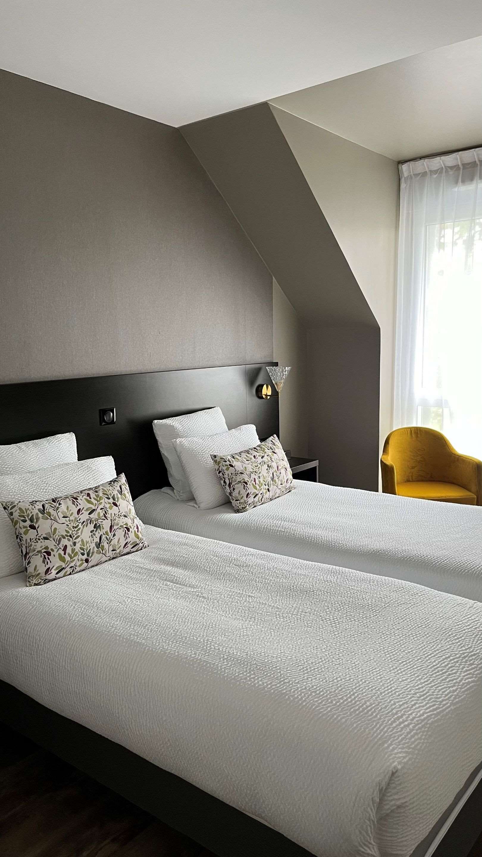 A modern hotel room with a large bed, a nightstand, a lamp, and a chair.