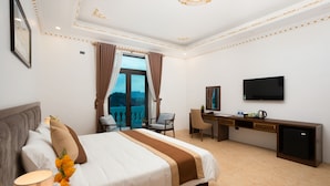 A hotel room with a large bed, a desk, a chair, a TV, and a view of the outdoors. - Trang An International Hotel (Tay Hoa Lu)