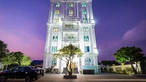 A multi-story hotel with a prominent entrance, a large tree in front, and a parking area with vehicles. - Trang An International Hotel (Tay Hoa Lu)