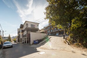 A residential street with modern buildings, a parked car, and a blue dumpster. - Nicobri Studios (Floresti)