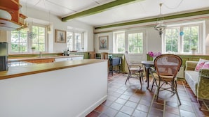 A spacious kitchen with a large island, wooden cabinets, and a dining area with wicker chairs and a table. - Cozy apartment in Sydals (Sydals)