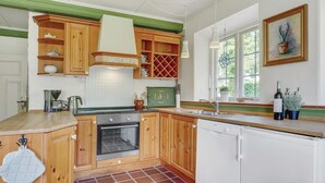 A kitchen with wooden cabinets, a Bosch dishwasher, a stove, and a window with a view of trees. - Cozy apartment in Sydals (Sydals)