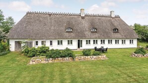A white cottage with a thatched roof, multiple windows, and a stone wall garden. - Cozy apartment in Sydals (Sydals)