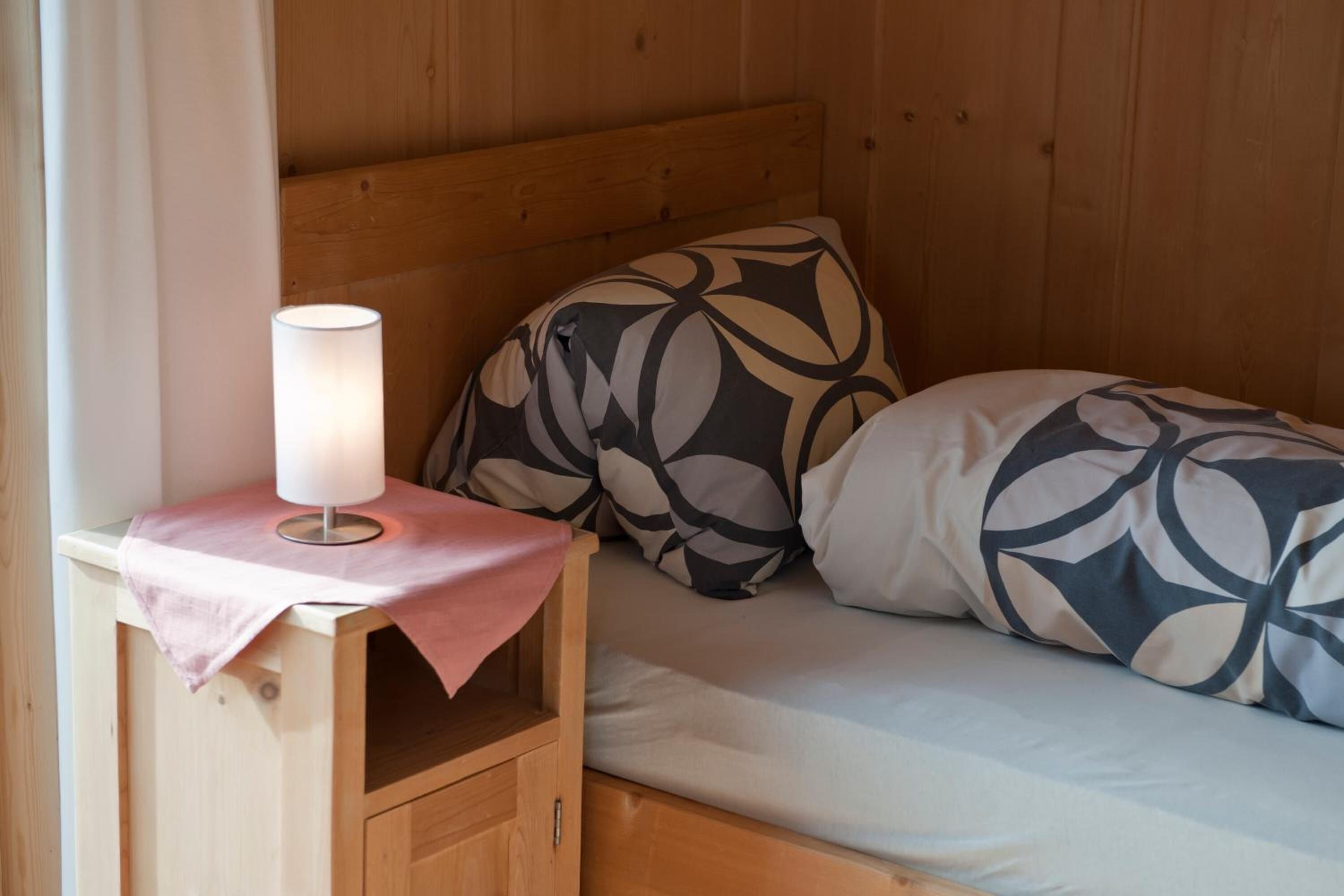 En træseng med køjeseng, et natbord og en lampe, med mønstrede puder og en lys madras.