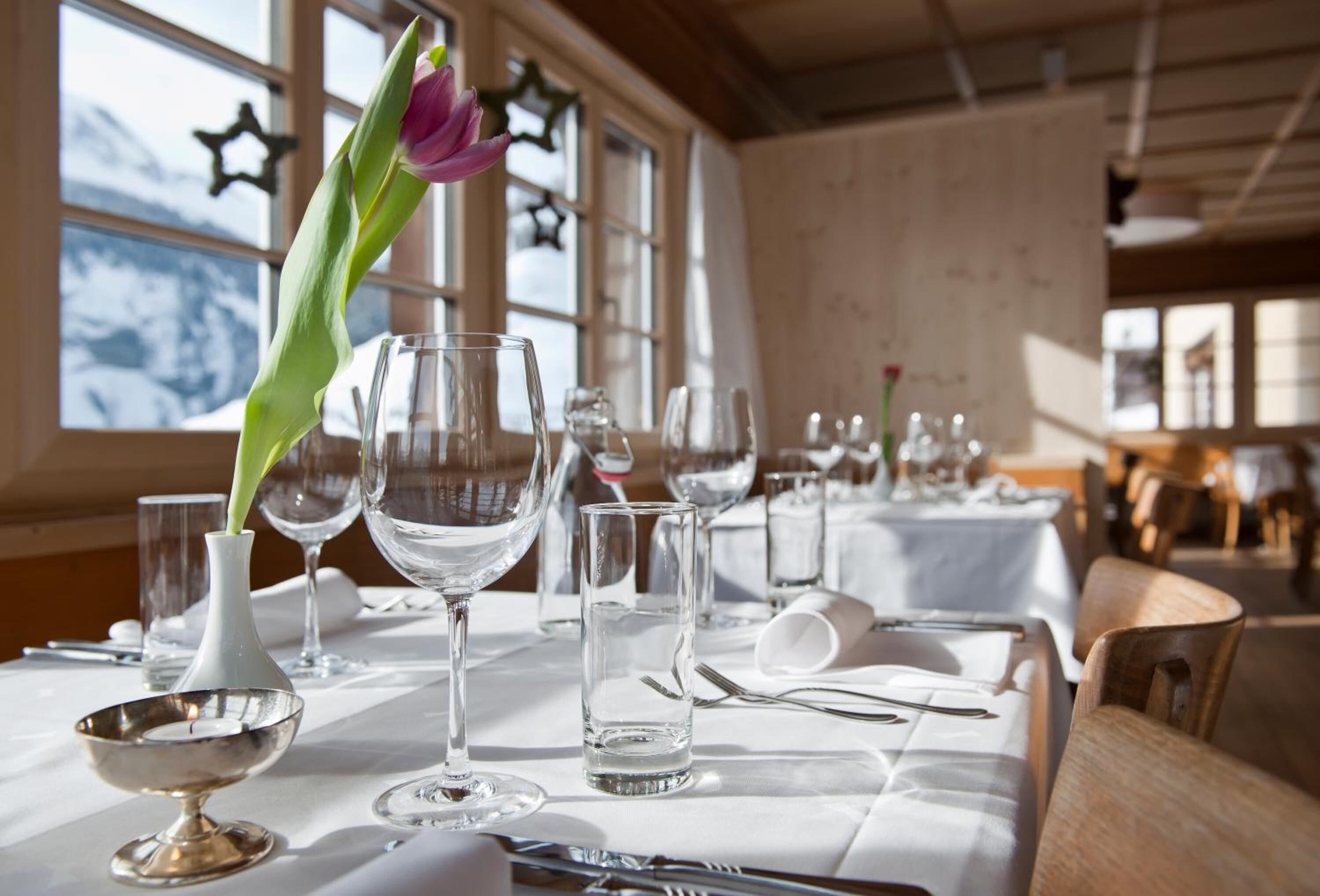 A dining table set with clear glassware, a silver bowl, and a vase with a single flower.