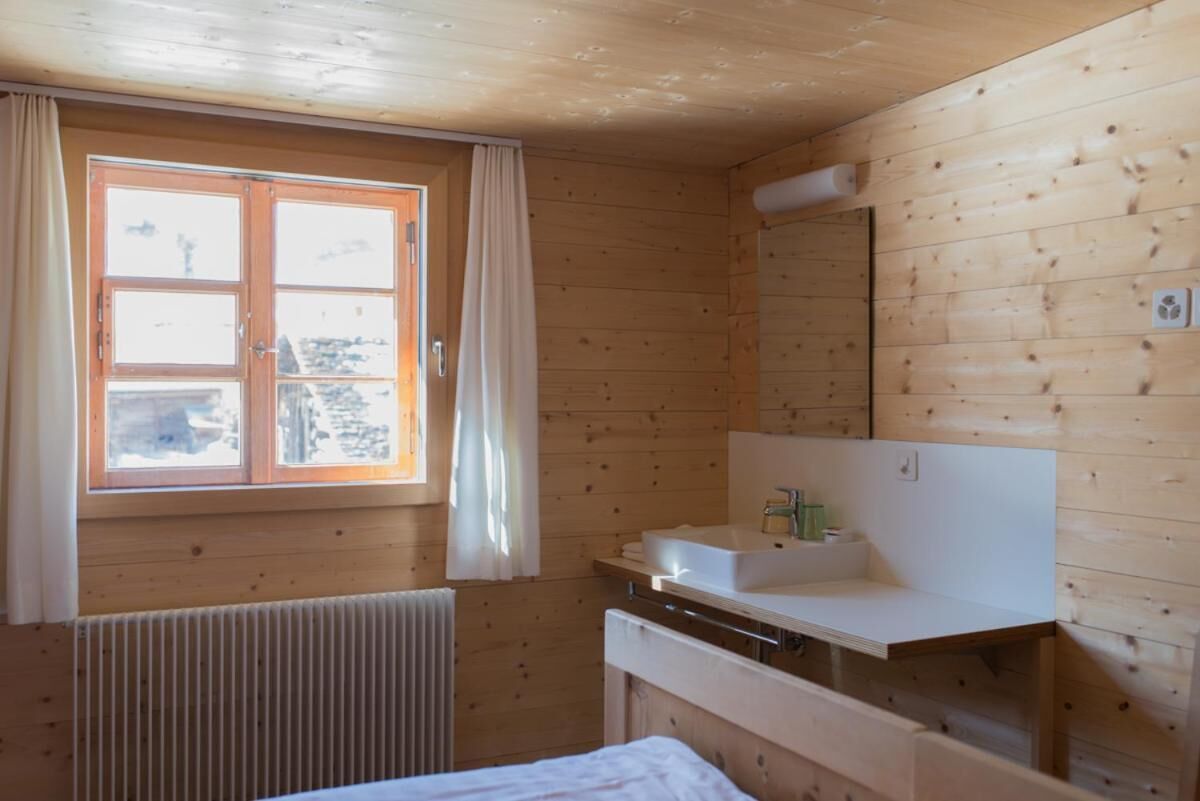 Quarto de cabana de madeira com janela, pia branca e radiador.