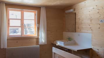 Quarto de cabana de madeira com janela, pia branca e radiador.