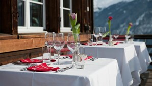 A table set for dining with clear glassware and red napkins, set against a backdrop of mountains and a wooden structure. - Hotel Restaurant Capricorns (Muntogna da Schons)