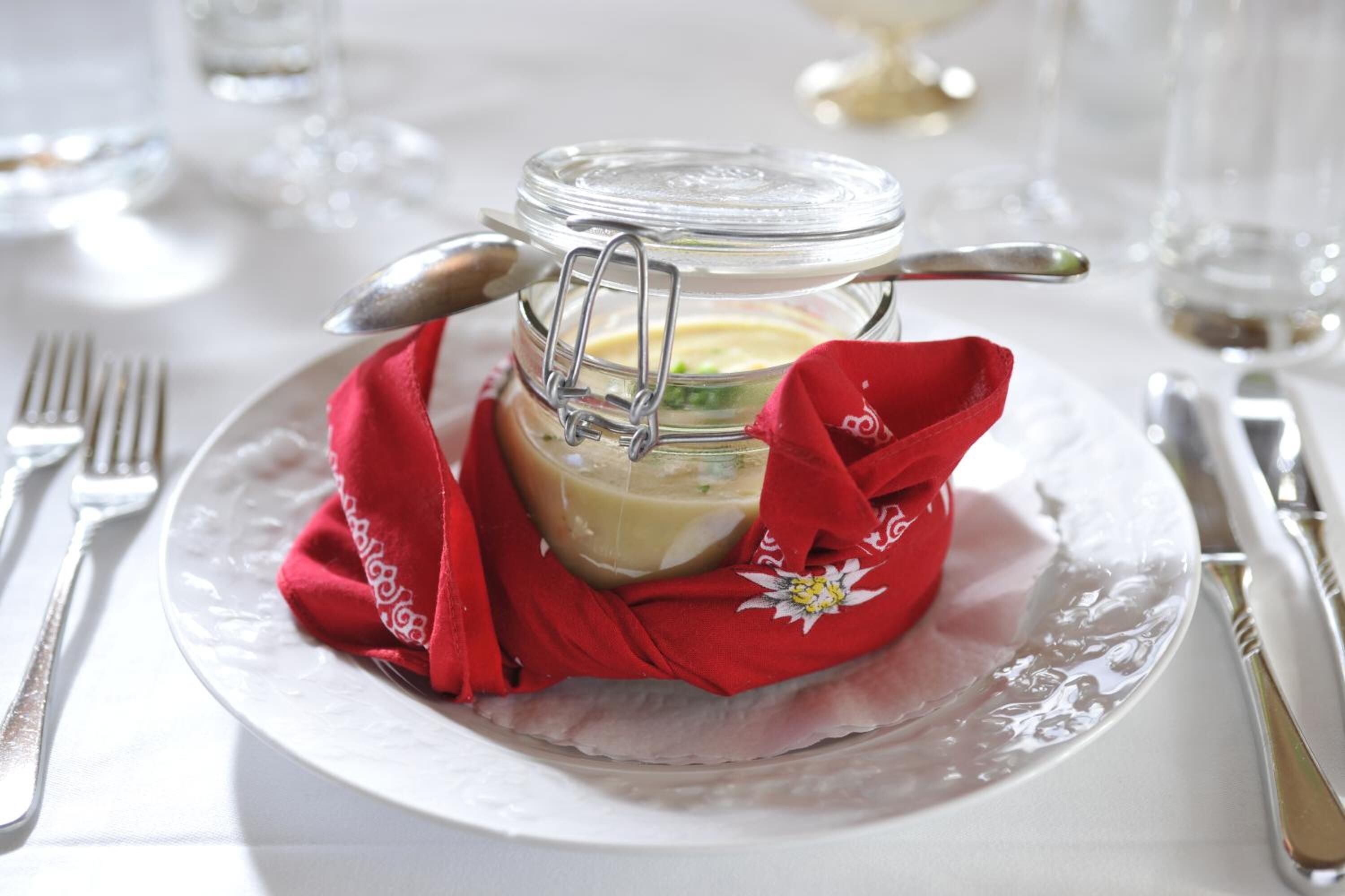 Un bocal en verre doté d’un couvercle métallique à fermoir, contenant une substance crémeuse, posé sur une assiette blanche avec une serviette en tissu rouge.