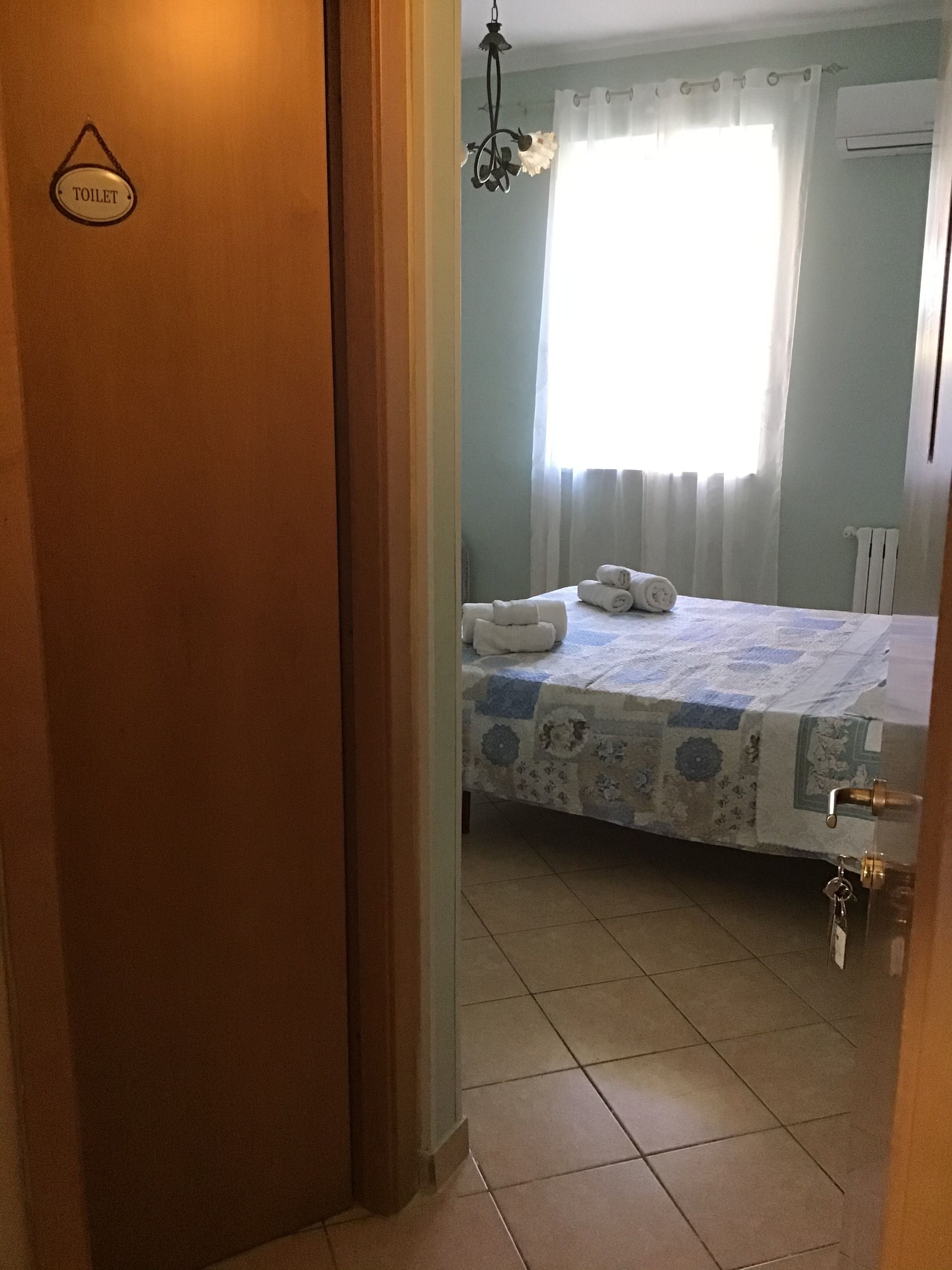 Une chambre d’hôtel avec un lit, une fenêtre avec des rideaux, un panneau indiquant les toilettes et un porte-clés accroché à la porte.