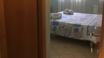 Une chambre d’hôtel avec un lit, une fenêtre avec des rideaux, un panneau indiquant les toilettes et un porte-clés accroché à la porte.