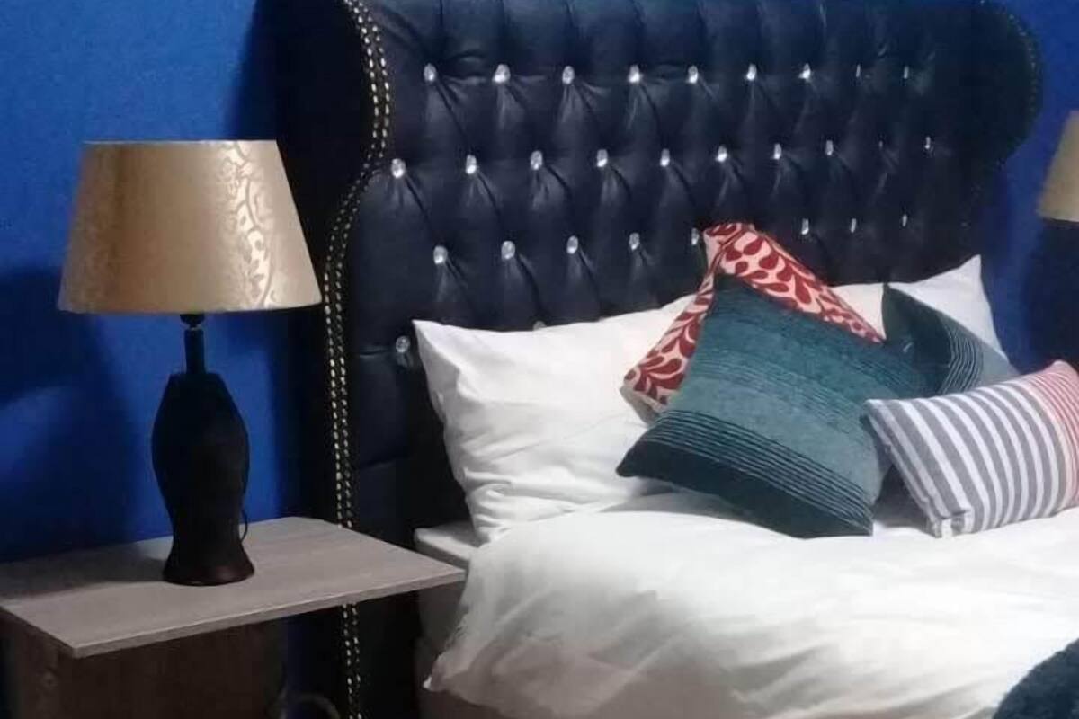 A bedroom with a tufted headboard, a bedside table with a lamp, a basket, and a blue patterned rug.