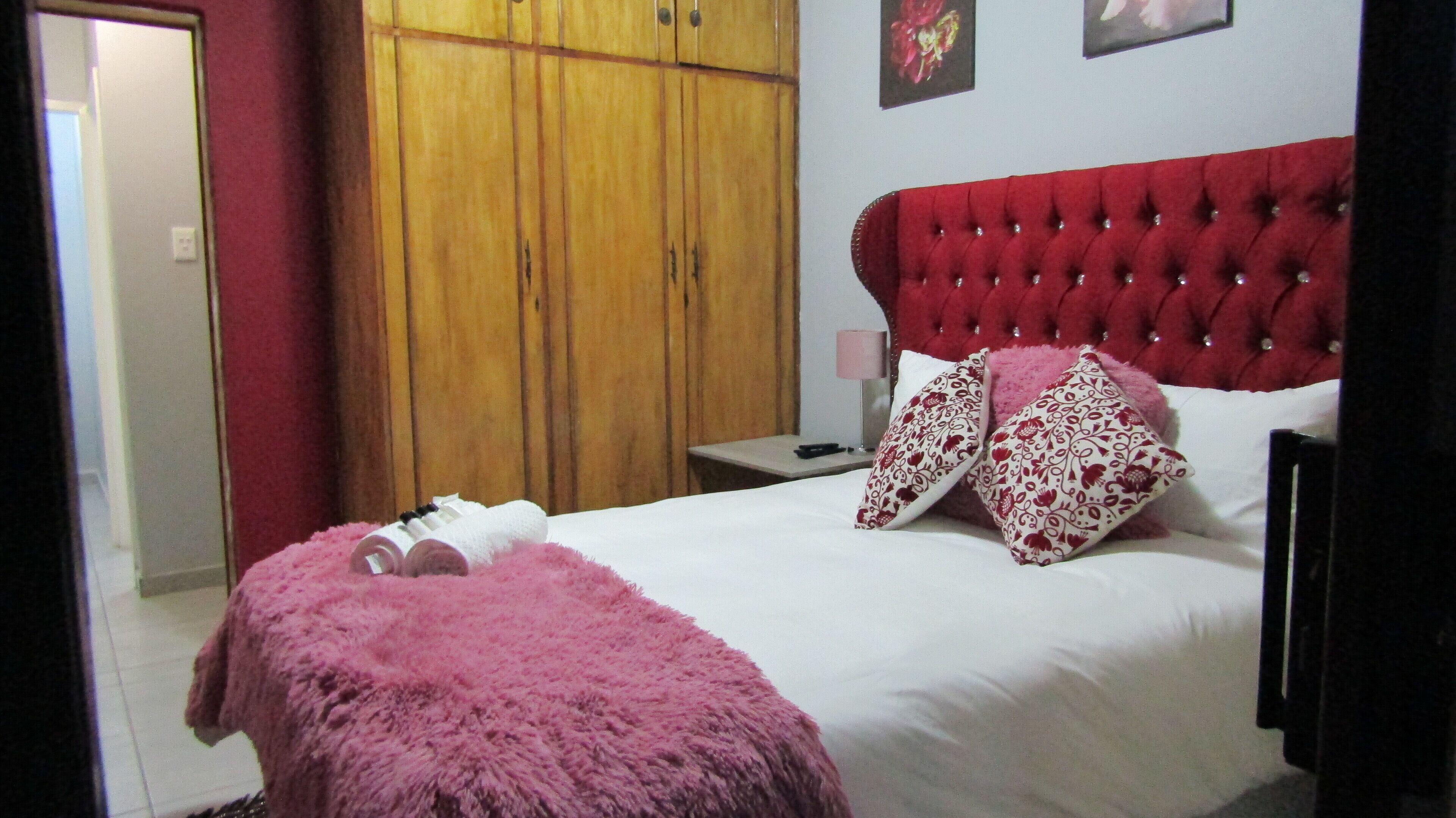 A bedroom with a large bed, a wooden wardrobe, a nightstand, and a red upholstered headboard.